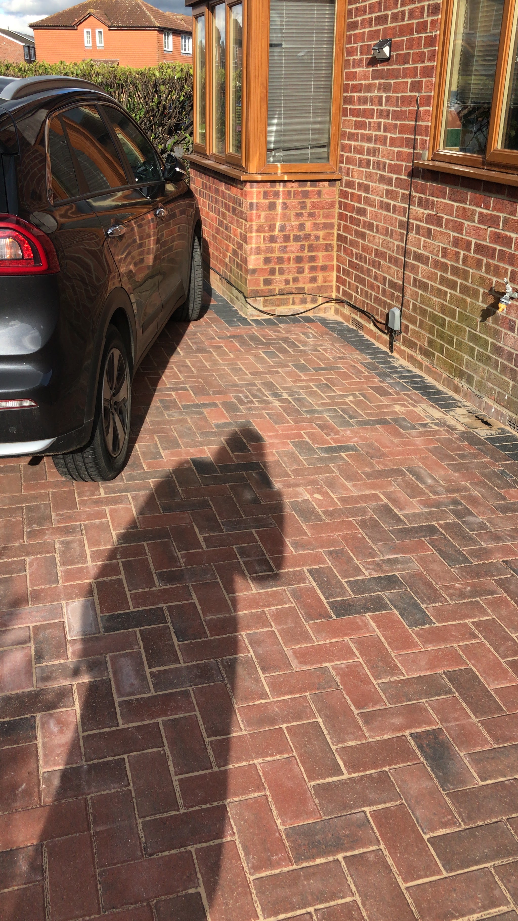A herringbone block paved driveway beside a red brick house with a car parked on it