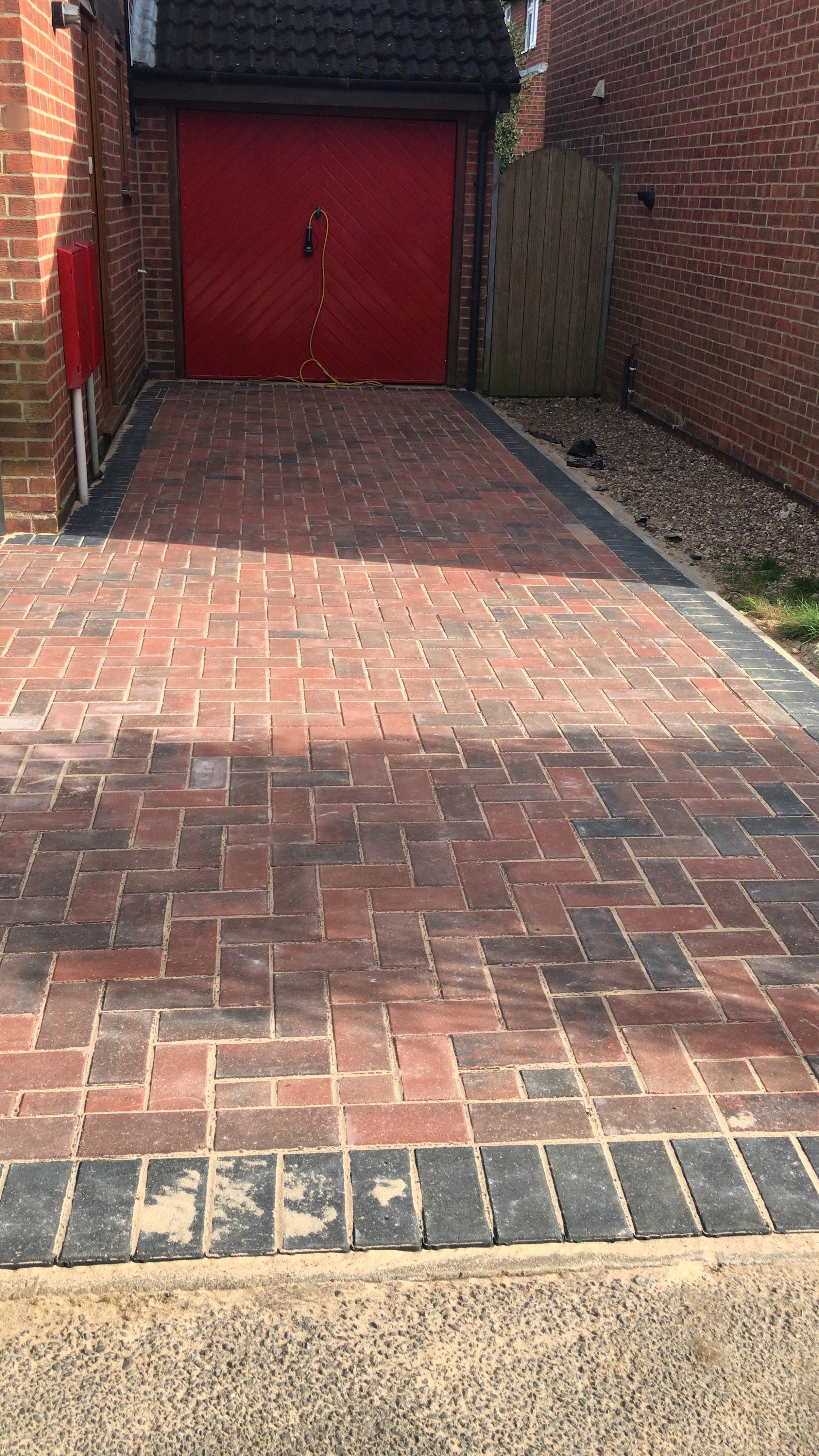 A herringbone block paved driveway leading up to a red garage door, edged with a charcoal border course