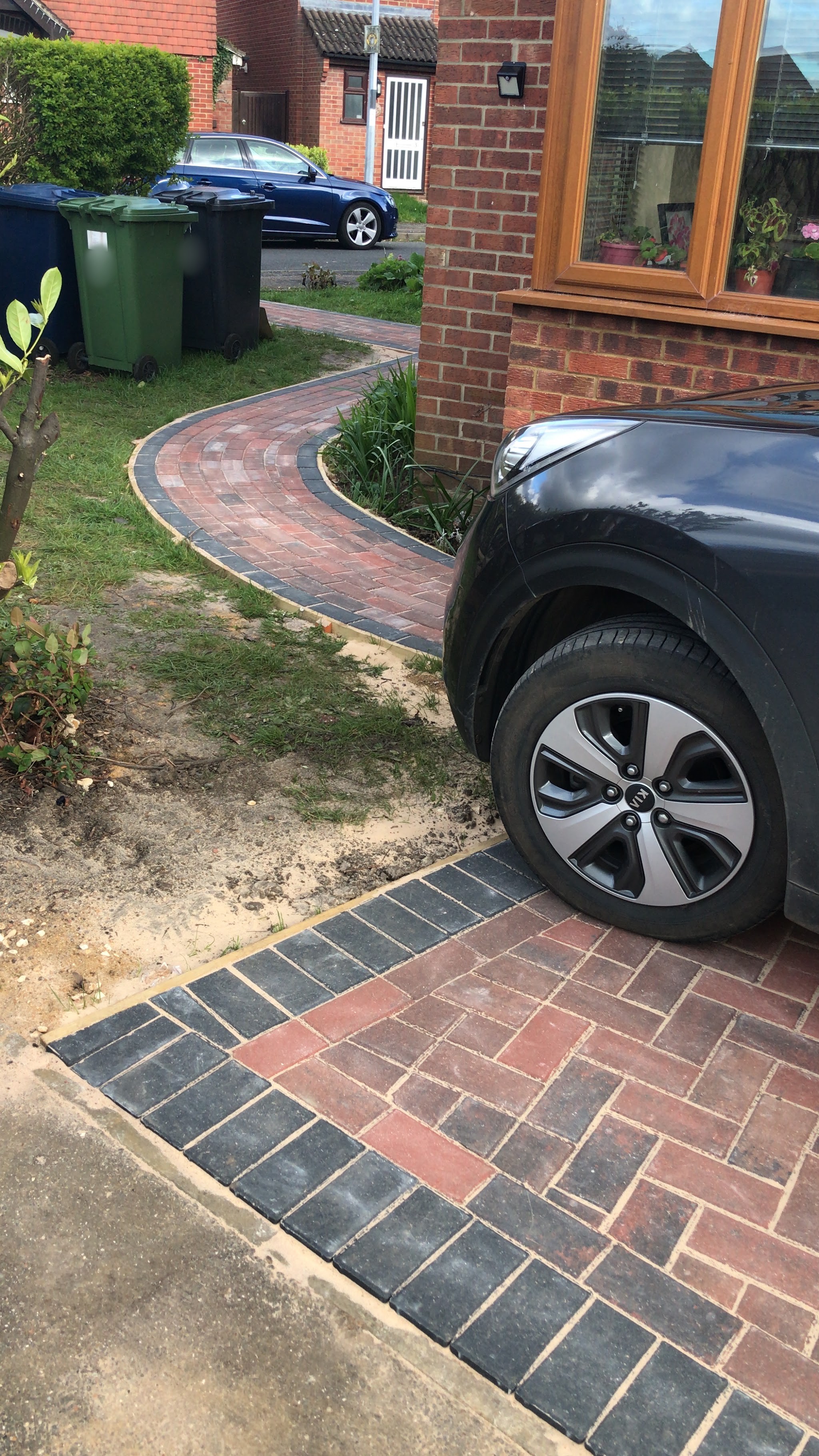 A curved block paved path with a charcoal border running round the side of a house