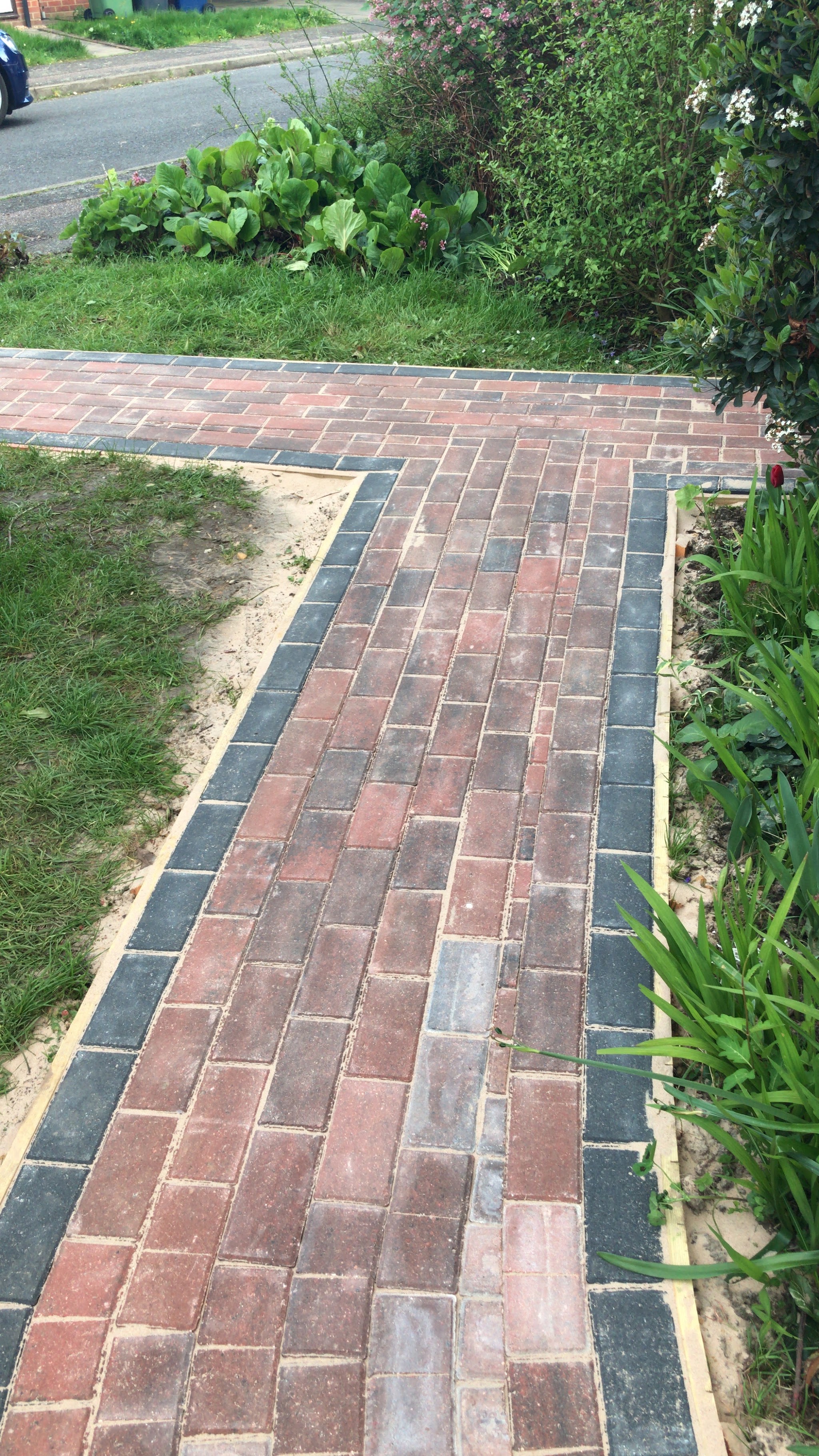 A straight block paved path edged in charcoal blocks beside a planted border